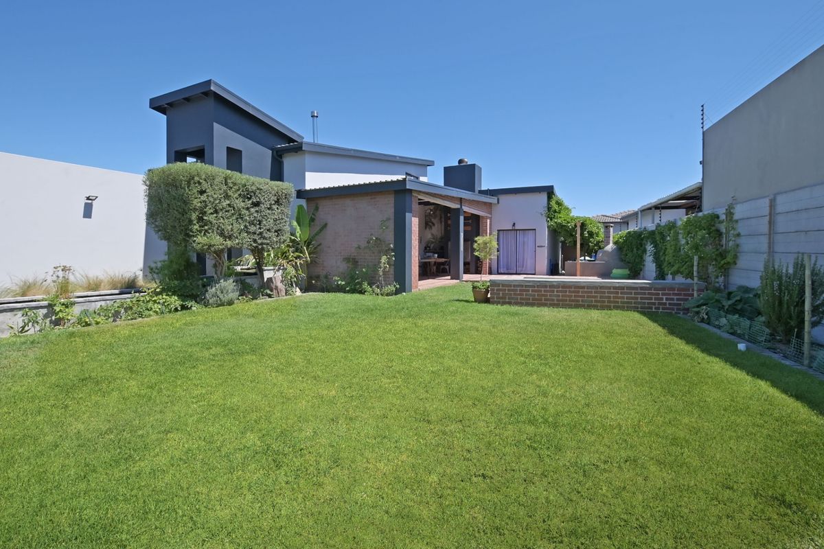 A well-maintained rear garden featuring a manicured lawn, a covered patio area, and a built-in brick outdoor oven.