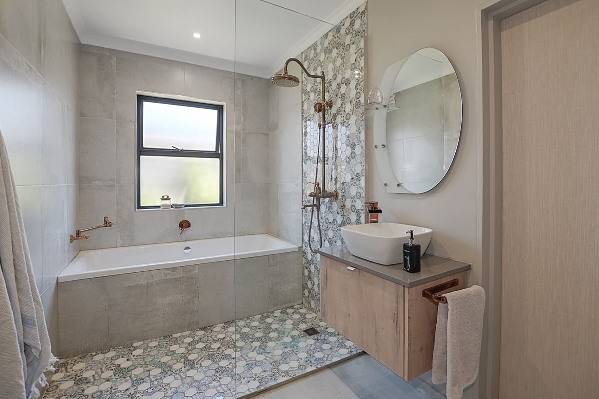 Modern bathroom featuring a built-in bathtub, glass shower screen, patterned tile accents, wall-mounted vanity with vessel sink, and contemporary copper-toned fixtures.