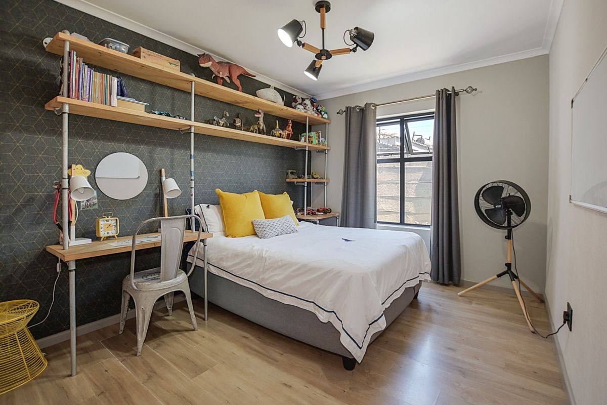 A well-maintained bedroom featuring wood-look flooring, a feature wallpaper wall, and a built-in industrial-style shelving and desk unit.