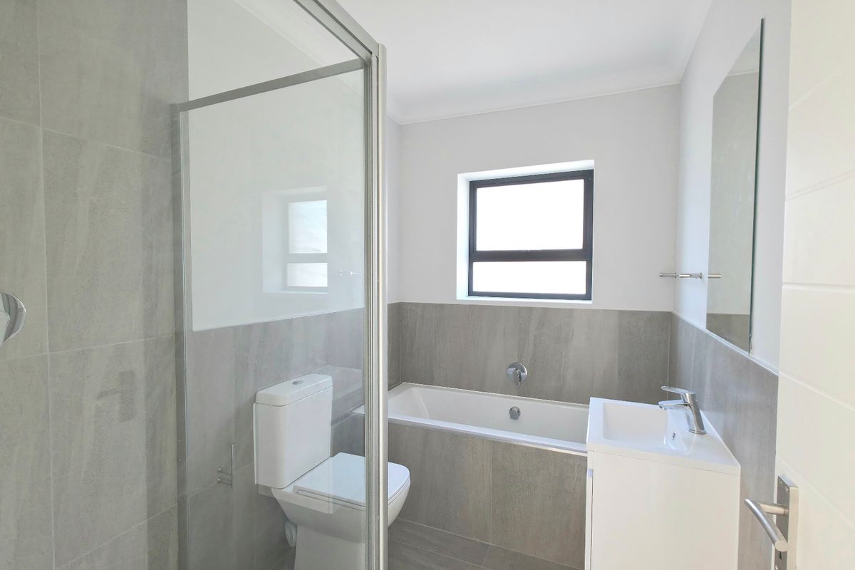 Modern bathroom featuring a glass-enclosed shower, built-in bathtub, vanity basin, and neutral grey tiling throughout.