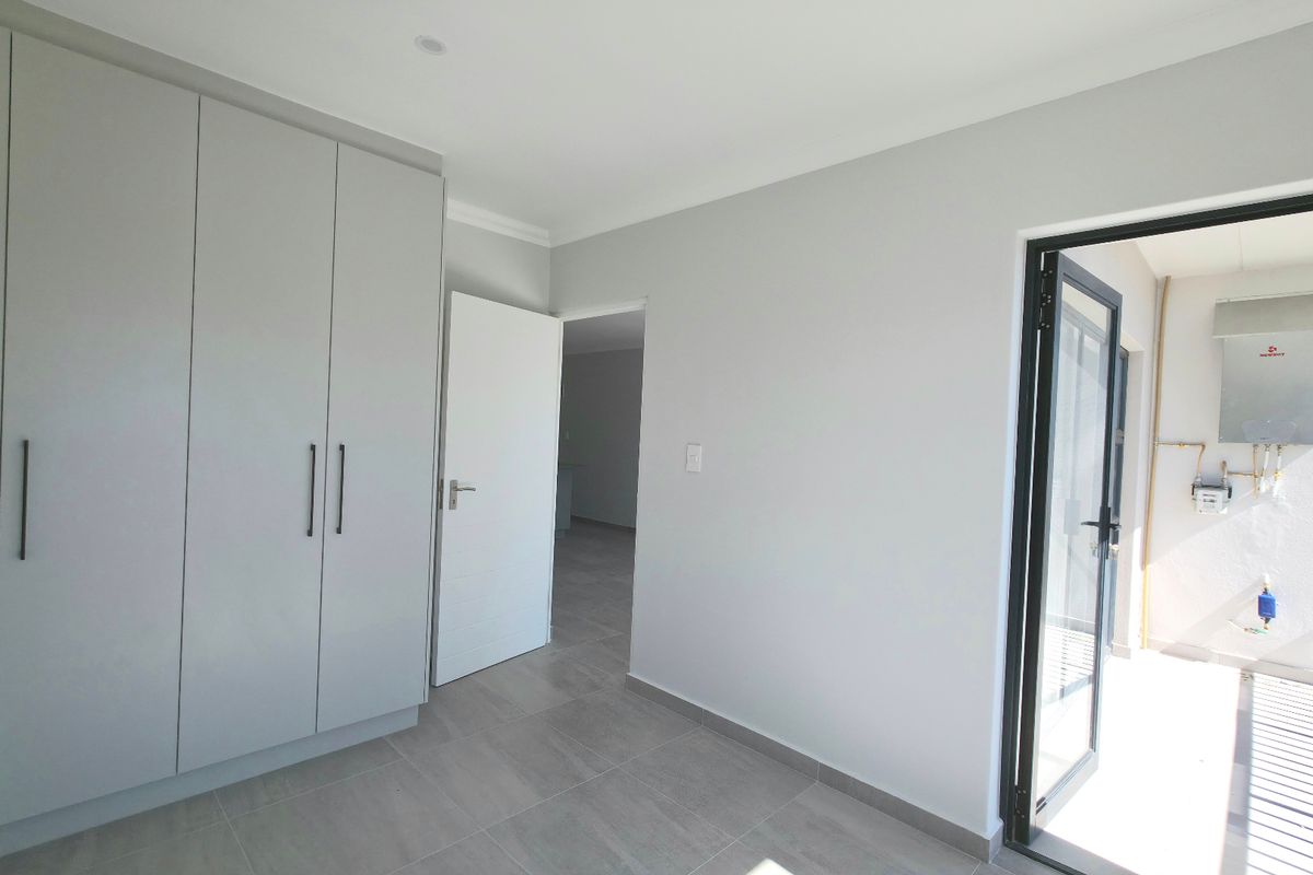 A bright, modern bedroom featuring neutral tiled flooring, ample built-in cupboard space, and direct access to an external utility area.
