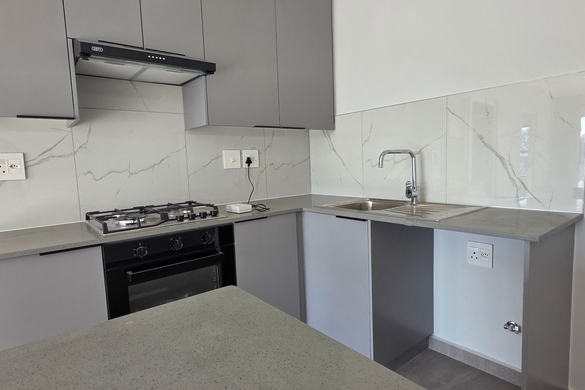 Modern kitchen featuring sleek grey cabinetry, stone countertops, a gas hob, built-in oven, and a stylish marble-look splashback.
