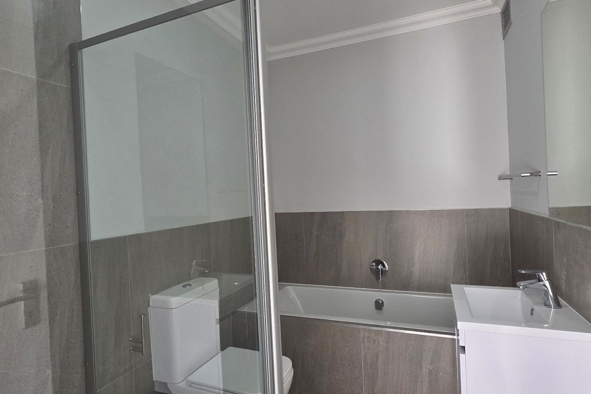 Modern bathroom featuring a glass-enclosed shower, built-in bathtub, vanity basin, and neutral grey wall tiling.