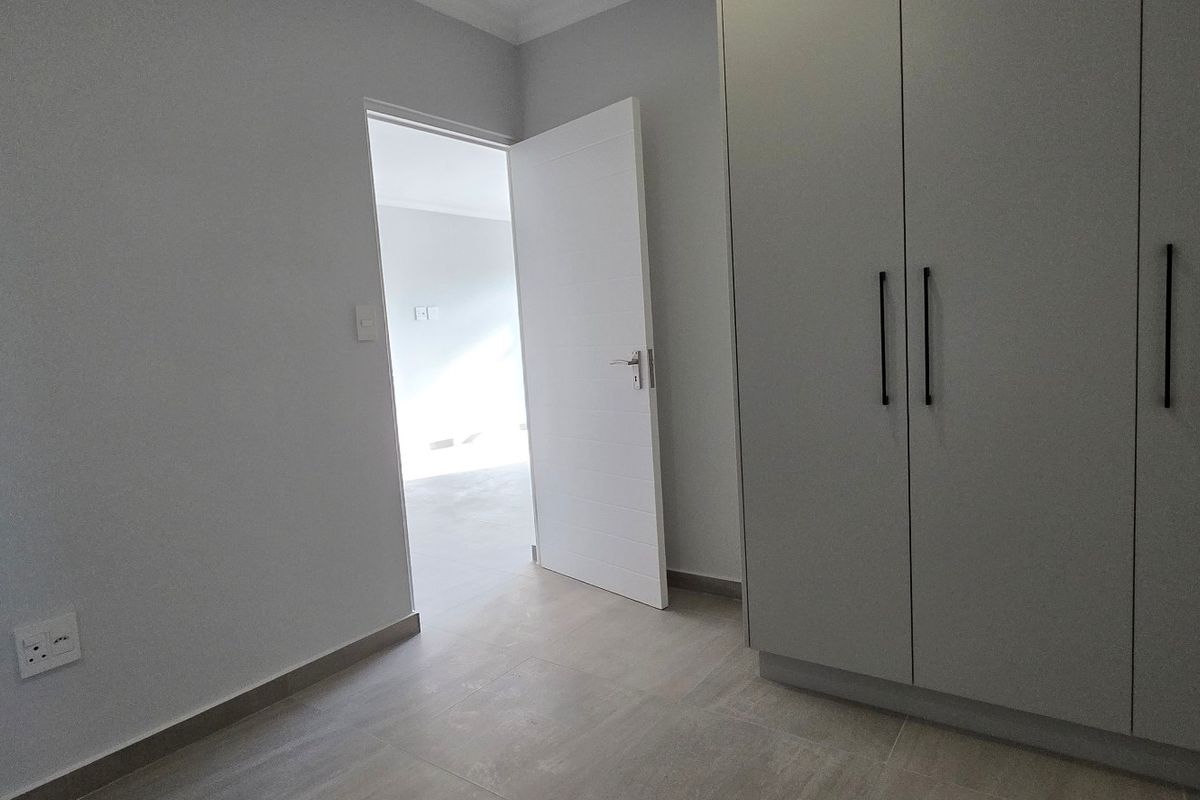 A clean, modern bedroom featuring neutral grey walls, tiled flooring, and built-in cupboards with contemporary black handles.