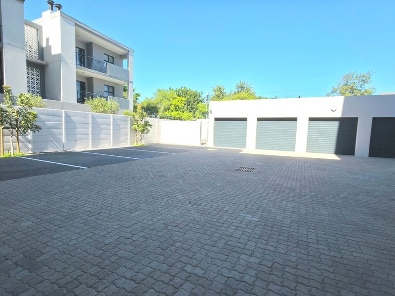 A well-maintained paved parking area featuring a triple garage and secure boundary walling within an apartment complex.