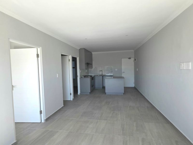 An open-plan living and kitchen area featuring modern grey cabinetry, a central island, and neutral tiled flooring throughout.