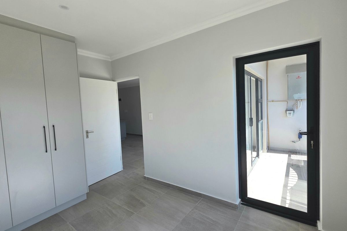 A bright, modern bedroom featuring neutral tiled flooring, ample built-in cupboard space, and direct access to an outdoor balcony area.