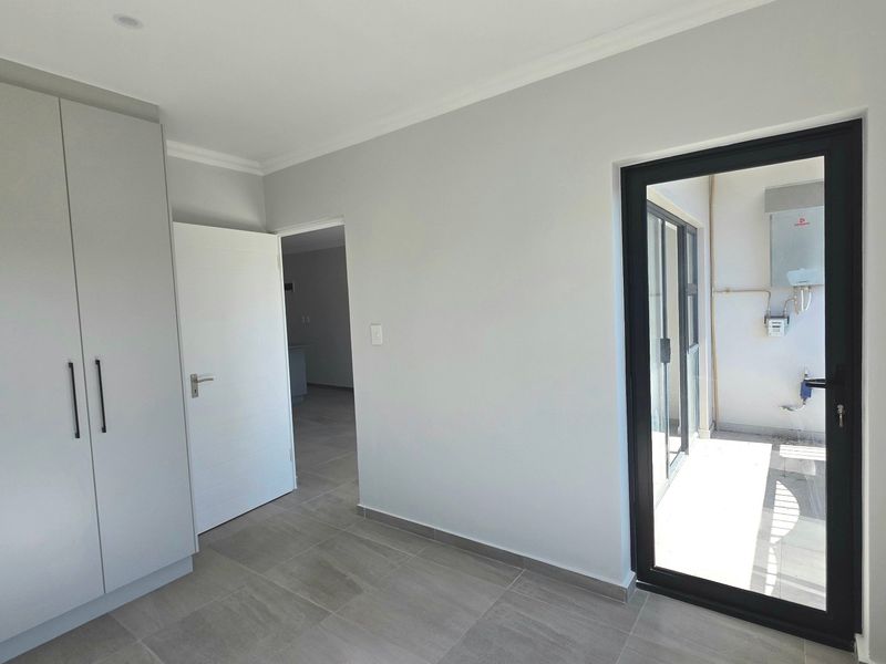 A bright, modern bedroom featuring neutral tiled flooring, ample built-in cupboard space, and direct access to an outdoor balcony area.