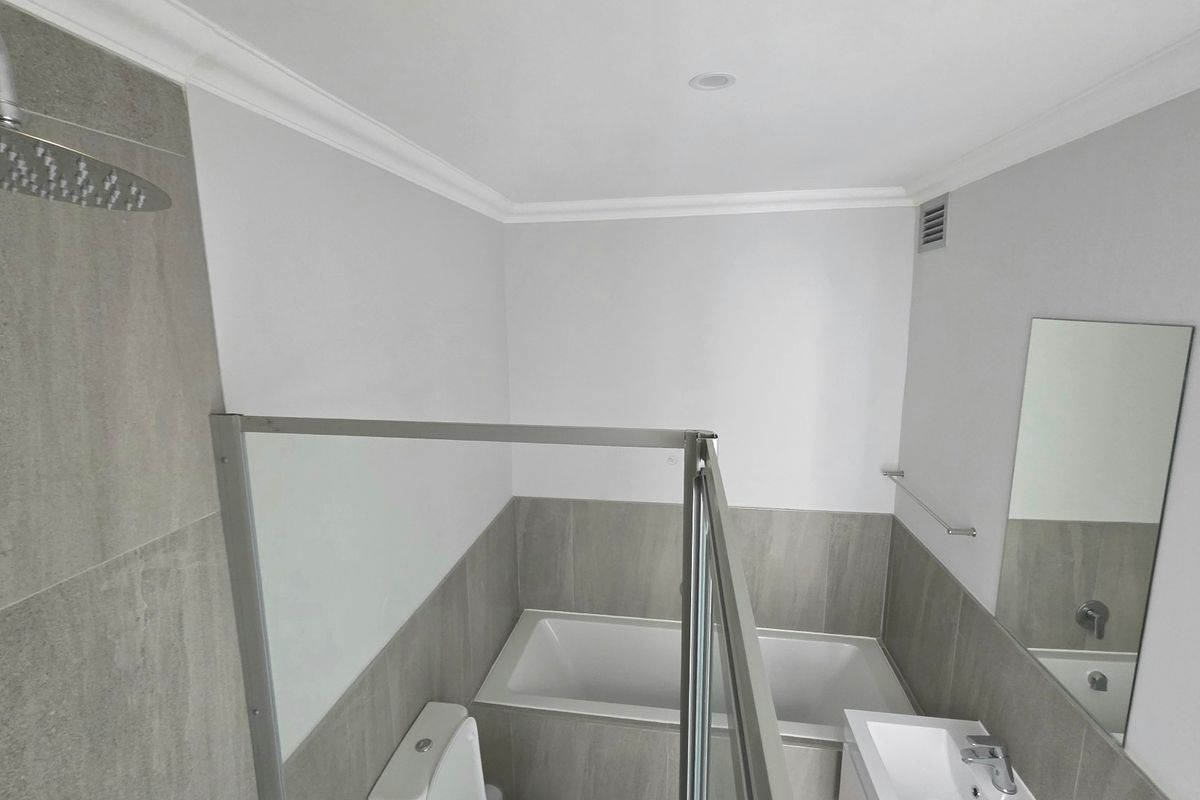 Modern bathroom featuring a built-in bathtub, glass-enclosed shower with rain shower head, vanity basin, and neutral grey tiling.