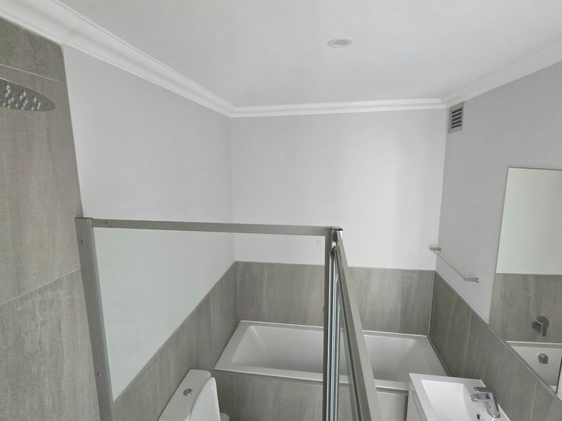 Modern bathroom featuring a built-in bathtub, glass-enclosed shower with rain shower head, vanity basin, and neutral grey tiling.
