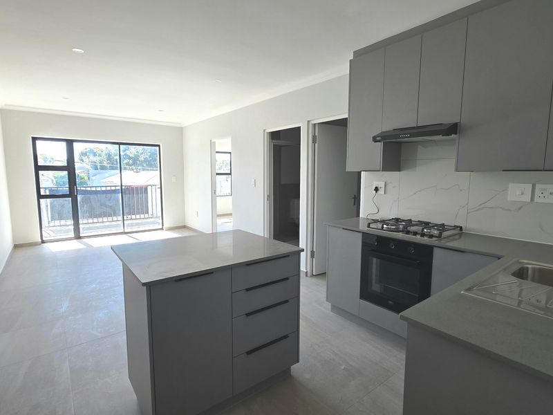 Modern open-plan kitchen and living area featuring sleek grey cabinetry, stone countertops, built-in appliances, and access to a private balcony.