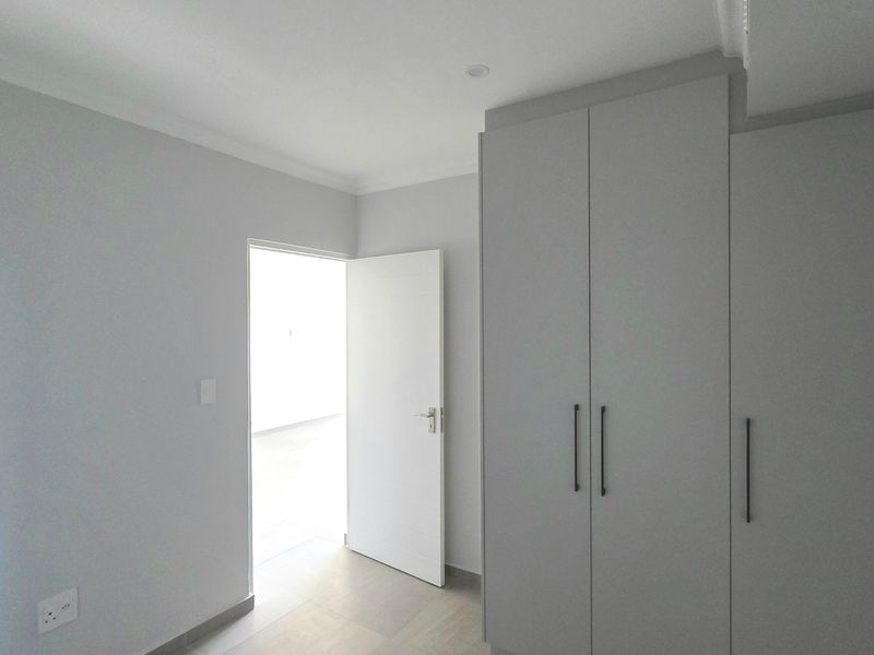 A clean, modern bedroom featuring neutral grey walls, built-in cupboards with contemporary handles, and recessed lighting.