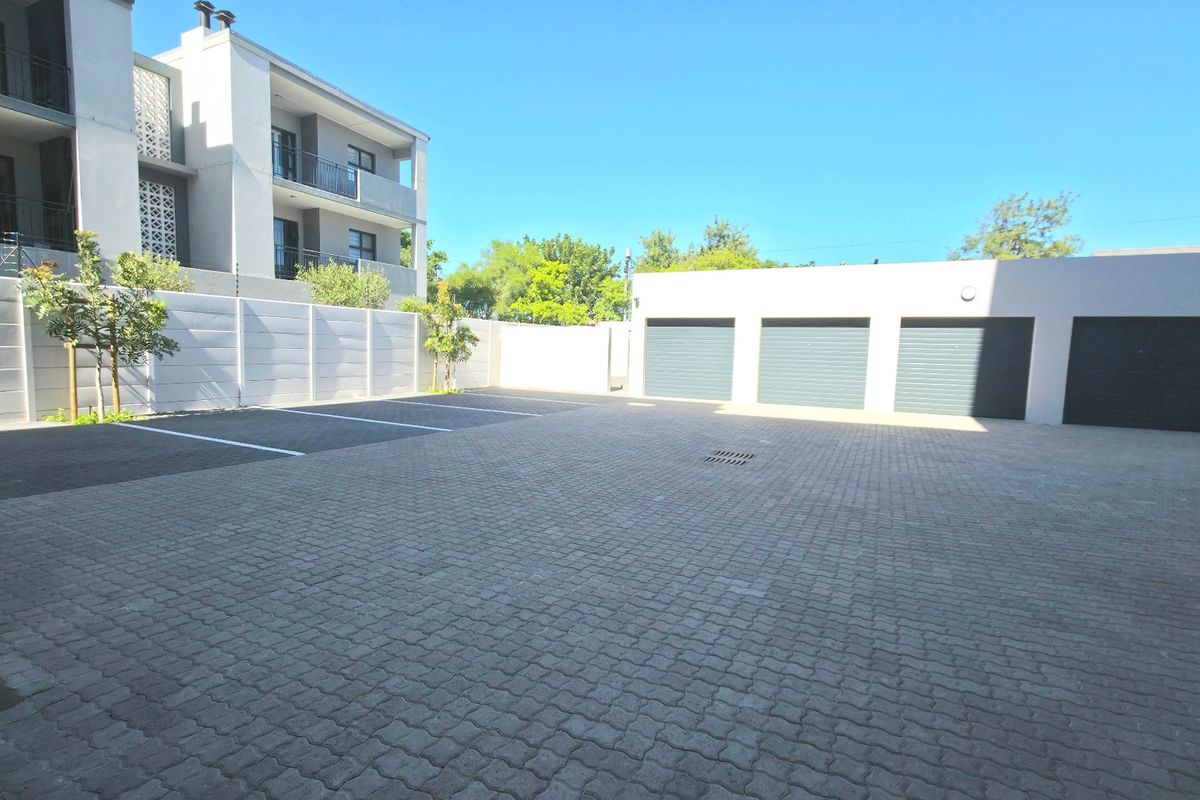 A well-maintained paved parking area featuring a triple garage and secure boundary walling within an apartment complex.