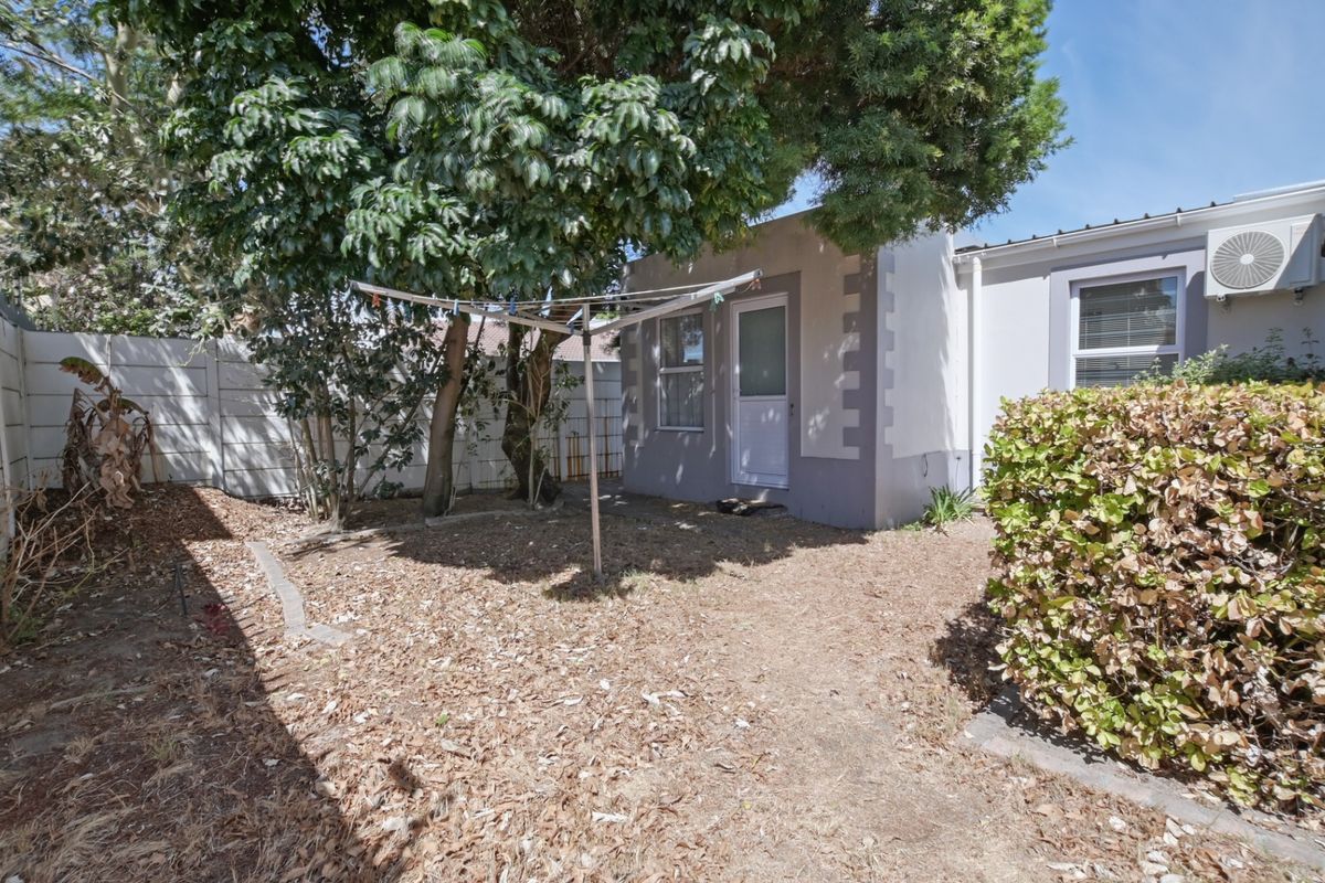 A rear exterior view of the property featuring a small garden area, mature trees, and a wall-mounted air conditioning unit.