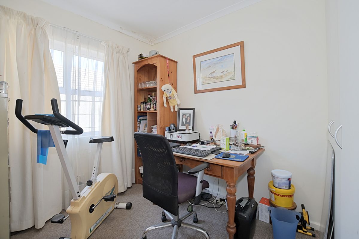 A functional bedroom or home office space featuring neutral walls, carpeted flooring, and a window with curtain treatments.