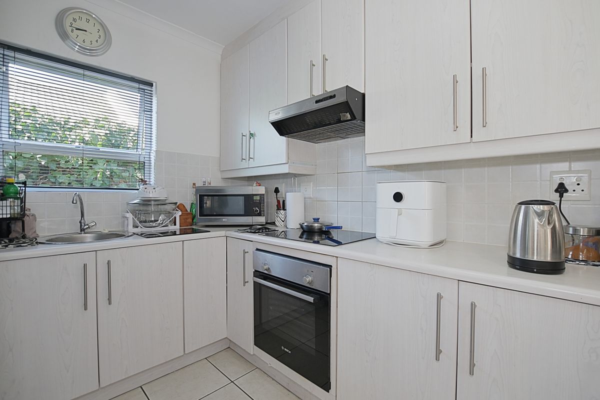 Compact kitchen featuring white laminate cabinetry, tiled splashback, built-in oven, electric cooktop, and stainless steel sink.