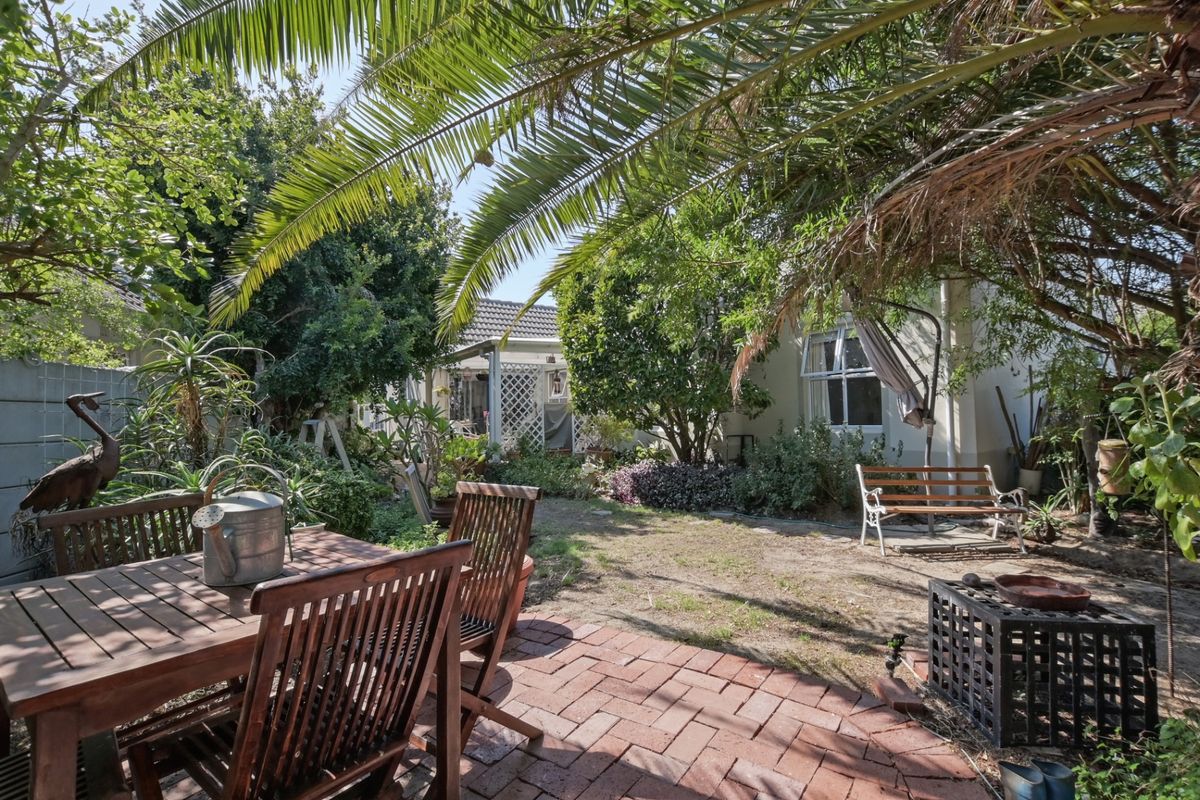 A private rear garden featuring a brick-paved patio area, mature palm trees, and established landscaping, providing a quiet outdoor space.