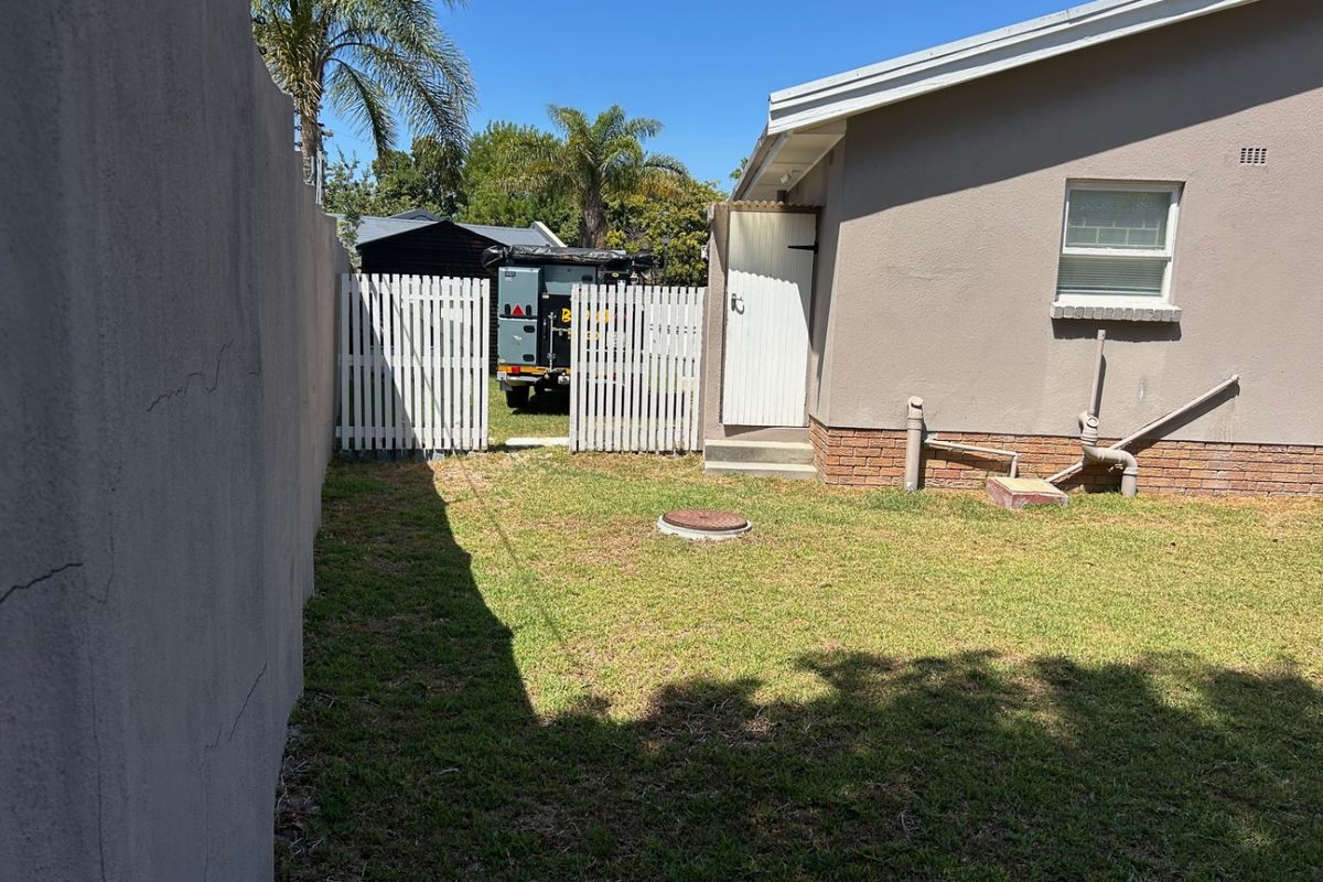 A view of the rear garden area featuring a lawn, boundary wall, and access to the side of the house with exterior plumbing fixtures.