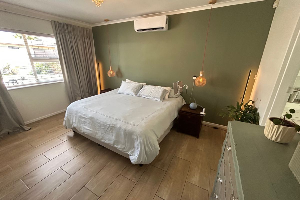 A well-maintained bedroom featuring wood-look tile flooring, a feature wall, split-system air conditioning, and modern pendant lighting.