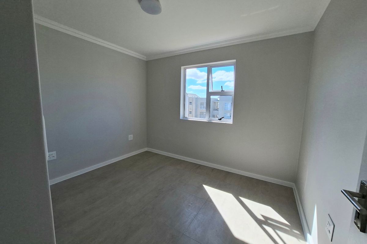 A bright, empty bedroom featuring neutral grey walls, modern tiled flooring, and a window providing natural light.