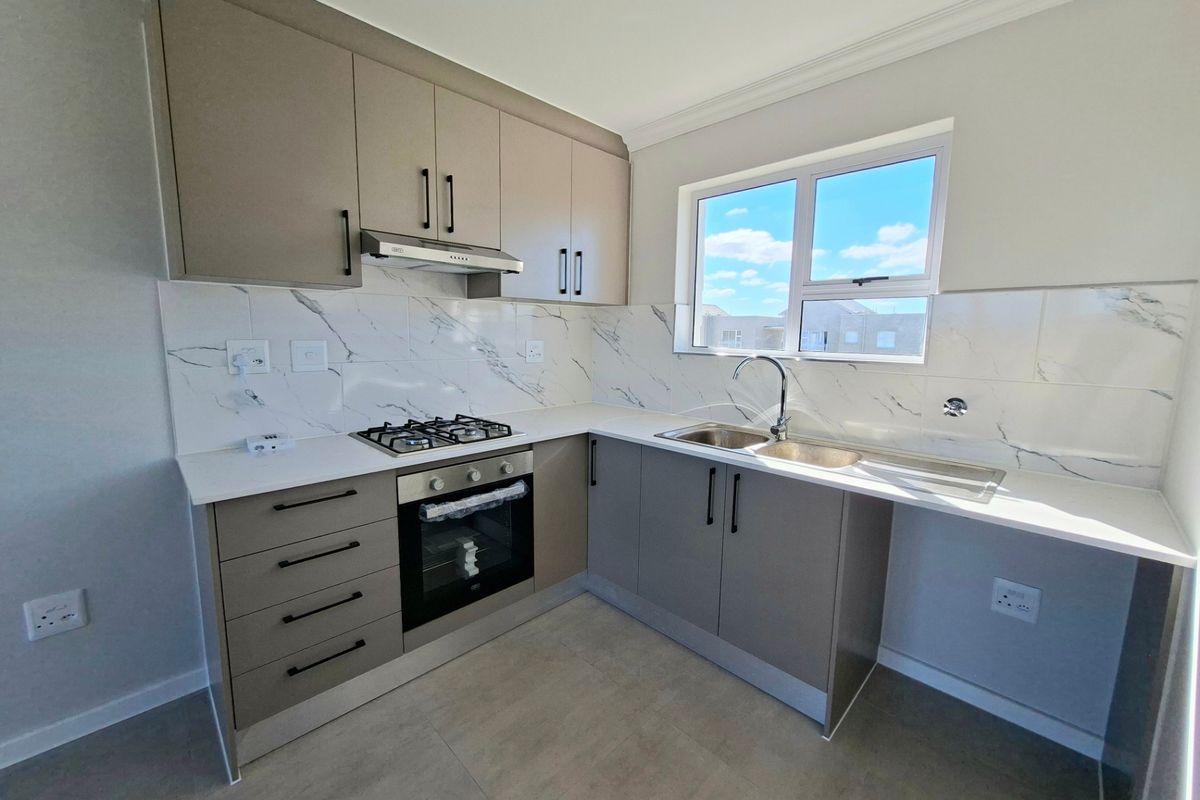Modern kitchen featuring sleek cabinetry, marble-look tiled backsplash, built-in oven, gas hob, extractor fan, and a double sink with a window view.