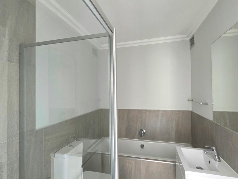 Modern bathroom featuring a glass shower enclosure, built-in bathtub, vanity basin with chrome fixtures, and neutral wall tiling.