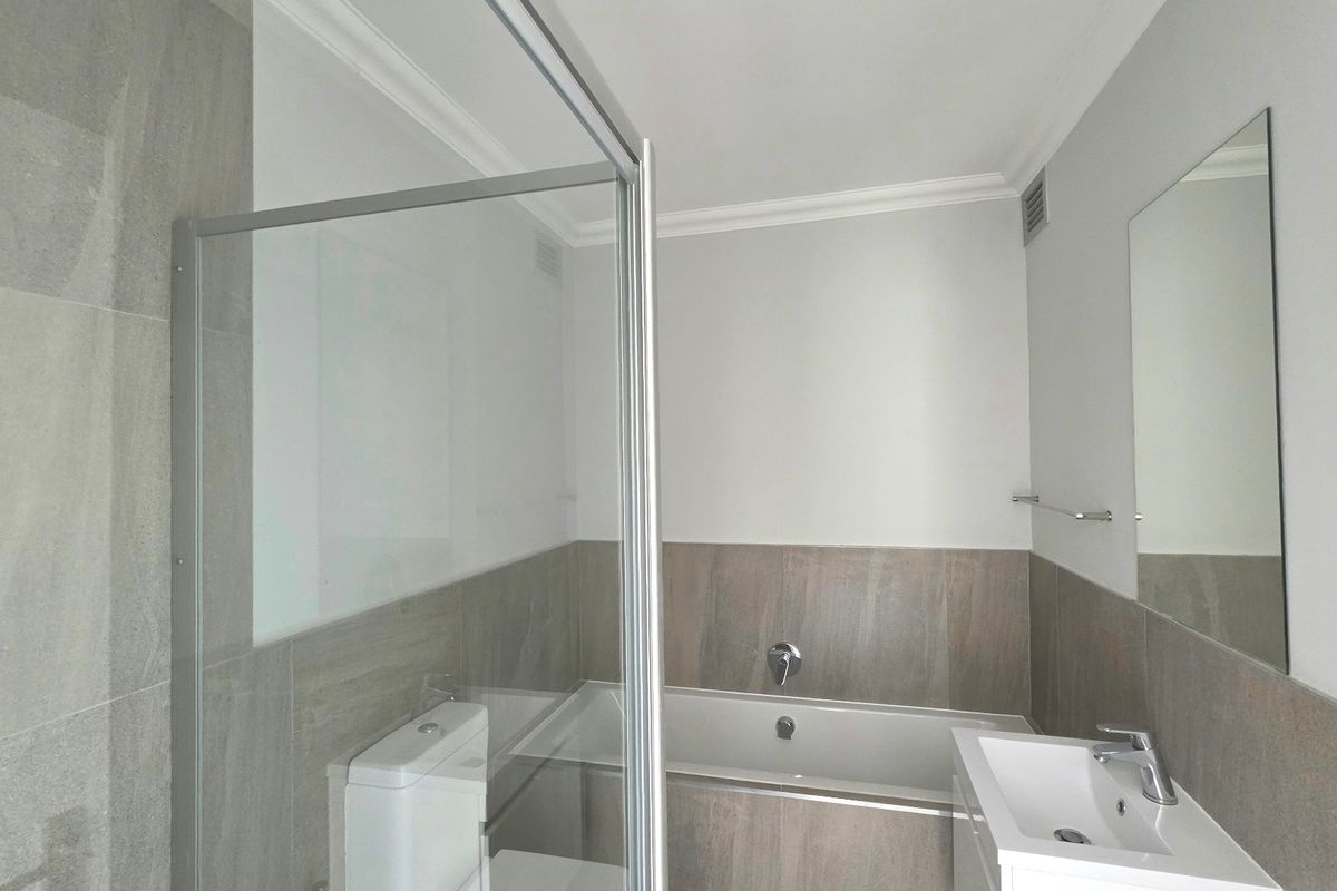 Modern bathroom featuring a glass shower enclosure, built-in bathtub, vanity basin with chrome fixtures, and neutral wall tiling.
