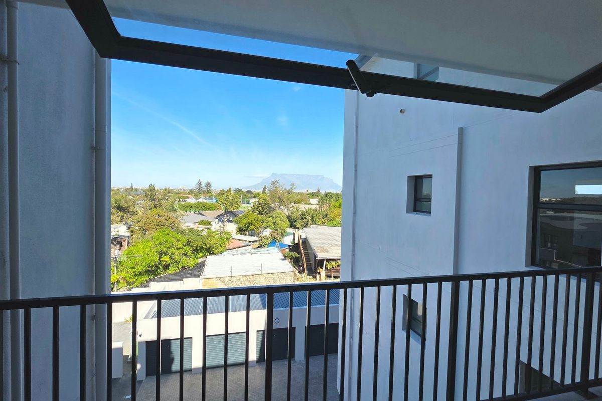 A private balcony featuring a metal balustrade and retractable awning, offering clear views of the surrounding neighborhood and distant mountain landscape.