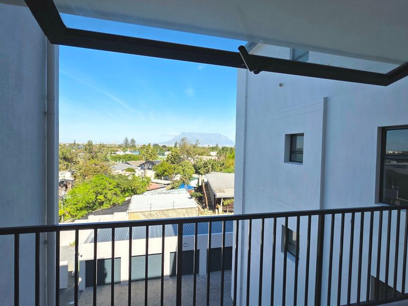 A private balcony featuring a metal balustrade and retractable awning, offering clear views of the surrounding neighborhood and distant mountain landscape.