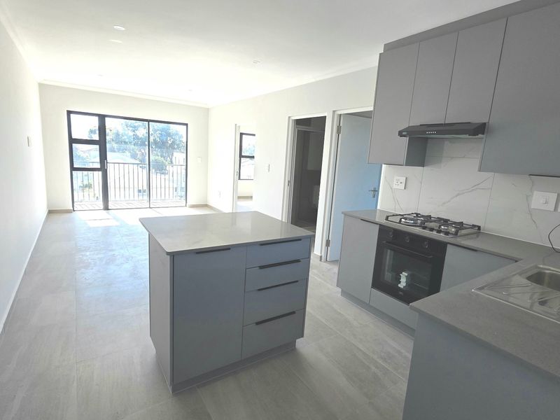 Modern open-plan living area featuring a sleek kitchen with grey cabinetry, stone countertops, built-in appliances, and a central island, leading to a balcony.