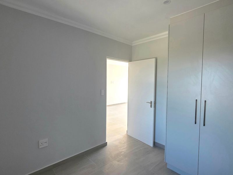 A clean, modern bedroom featuring neutral grey walls, tiled flooring, and ample built-in cupboard storage space.