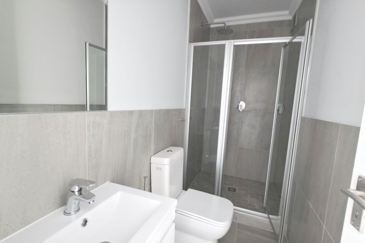 Modern bathroom featuring a glass-enclosed shower, vanity basin with chrome fixtures, and neutral floor-to-ceiling tiling.