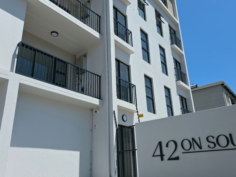 Exterior view of the 42 On South apartment complex, featuring modern white facade, private balconies with metal railings, and integrated security features.