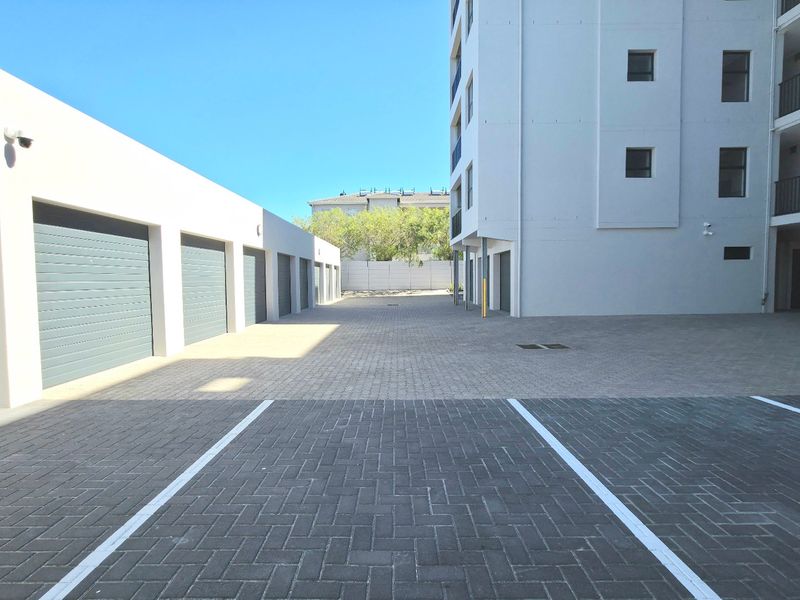 A clean, paved parking area and driveway serving the apartment complex, featuring multiple garage units and building access points.