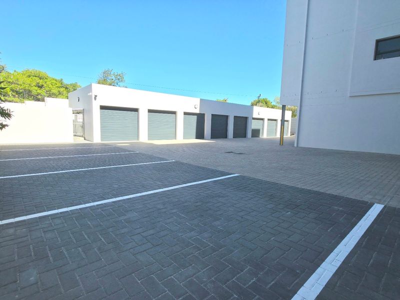 A well-maintained exterior area featuring a row of secure roller shutter garages and clearly marked paved parking bays.