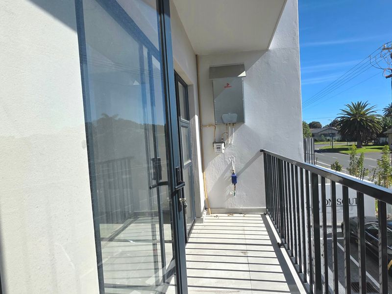 A clean, modern balcony featuring tiled flooring, a metal balustrade, and a wall-mounted gas geyser unit.