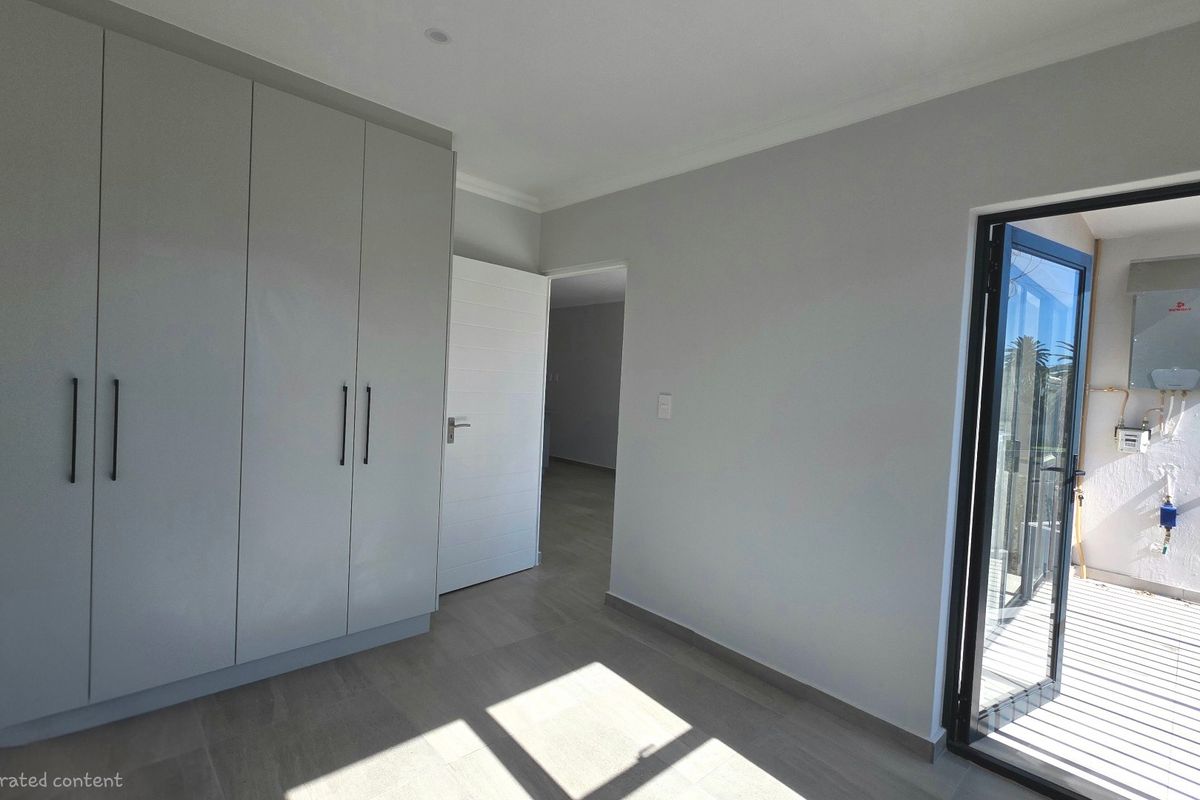 A bright, empty bedroom featuring modern built-in cupboards, neutral tiled flooring, and direct access to an outdoor balcony area.