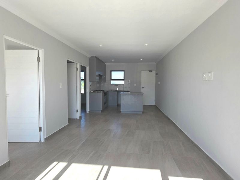 A bright, modern open-plan living and kitchen area featuring neutral grey tones, tiled flooring, and contemporary built-in cabinetry with integrated appliances.