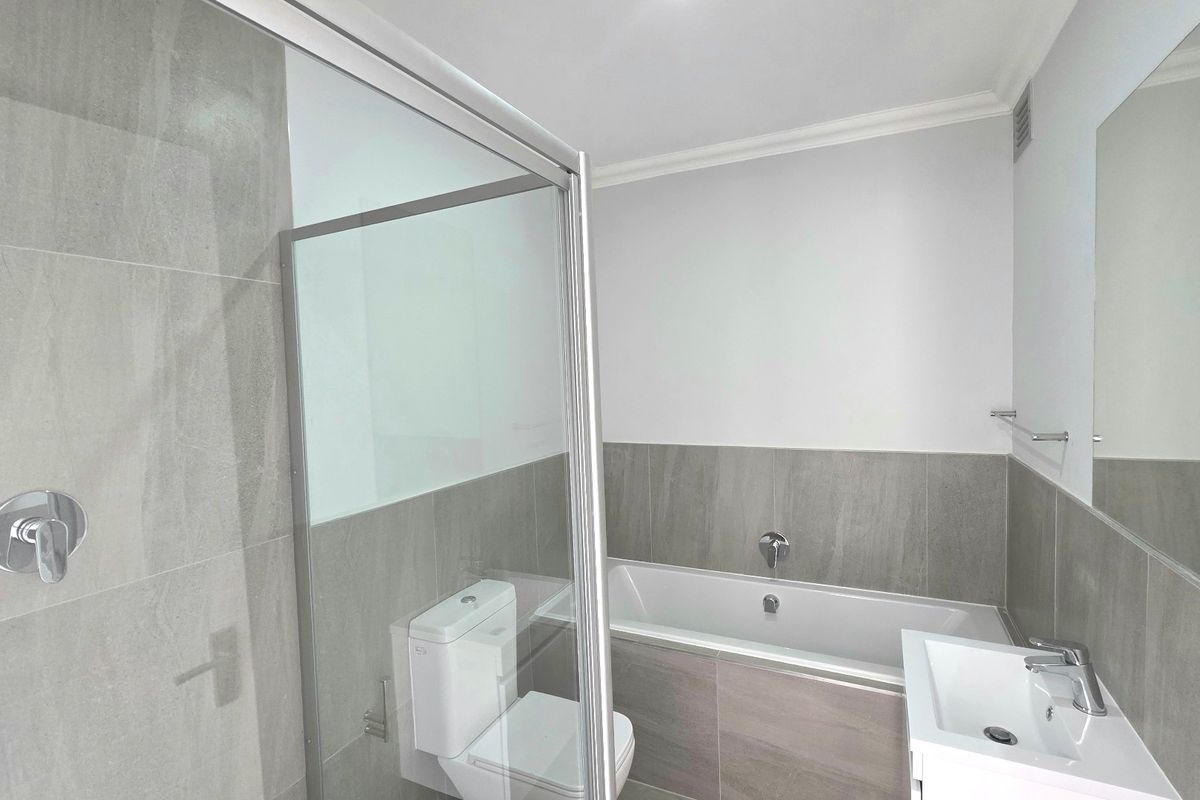 Modern bathroom featuring a glass-enclosed shower, built-in bathtub, vanity basin, and neutral grey wall tiling.