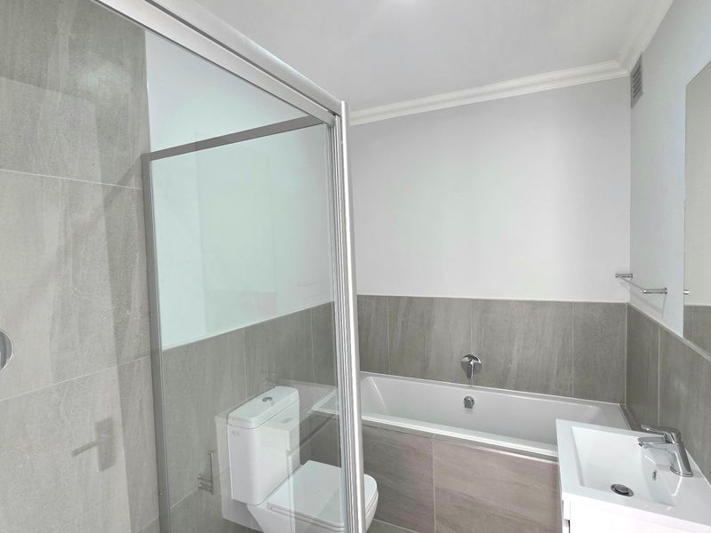Modern bathroom featuring a glass-enclosed shower, built-in bathtub, vanity basin, and neutral grey wall tiling.