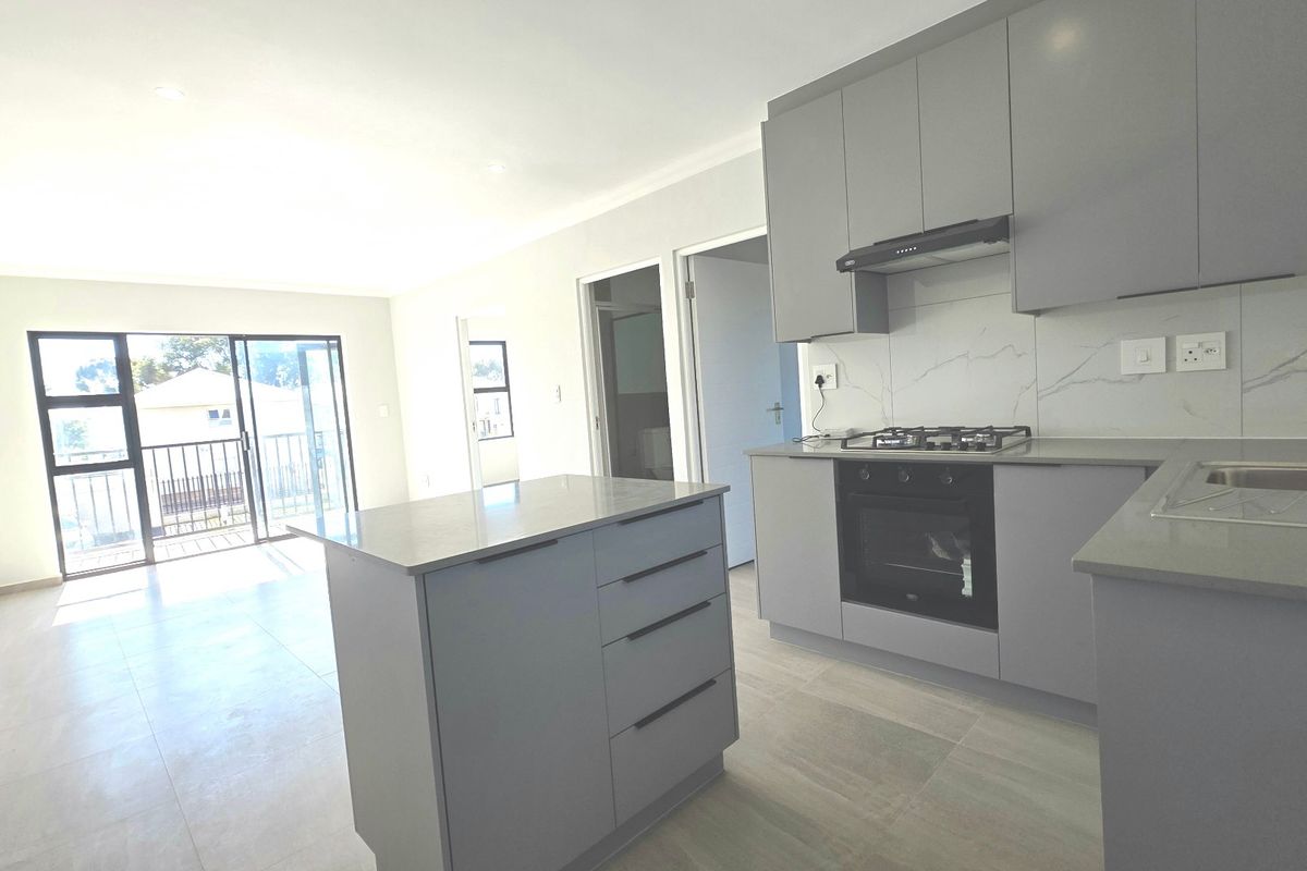 Modern open-plan kitchen and living area featuring sleek grey cabinetry, stone countertops, built-in appliances, and sliding doors leading to a balcony.