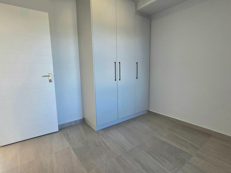 A clean, empty bedroom featuring modern tiled flooring and a built-in wardrobe with sleek handles.