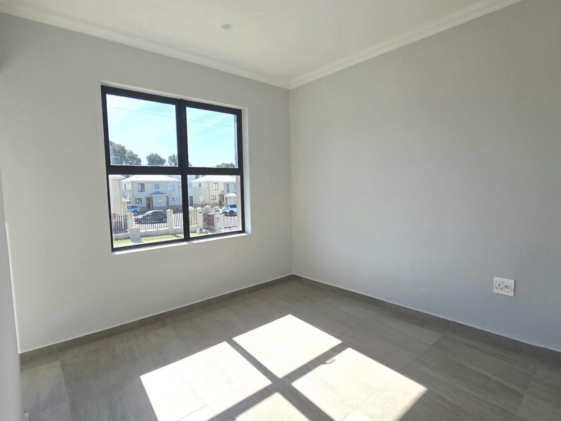 A bright, empty bedroom featuring neutral grey walls, tiled flooring, and a modern aluminium-framed window.