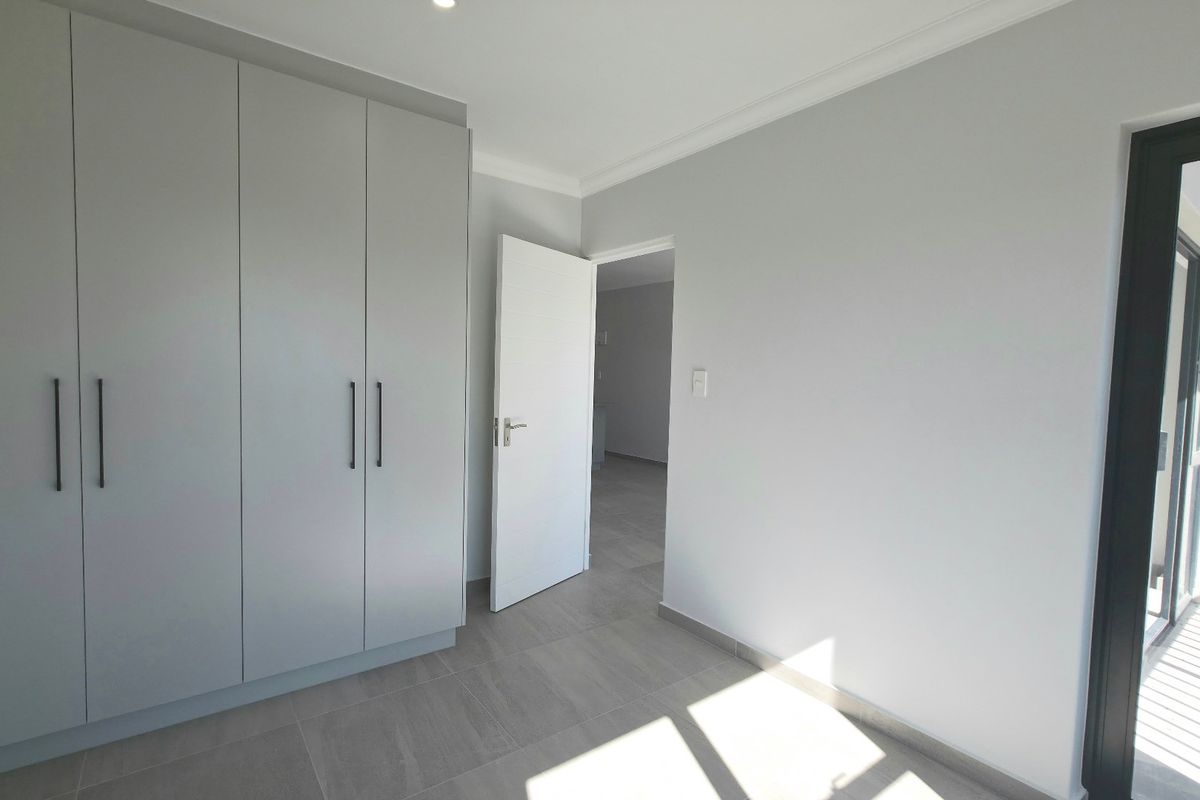 A bright, modern bedroom featuring neutral tiled flooring, built-in cupboards, and a sliding door leading to an outdoor area.