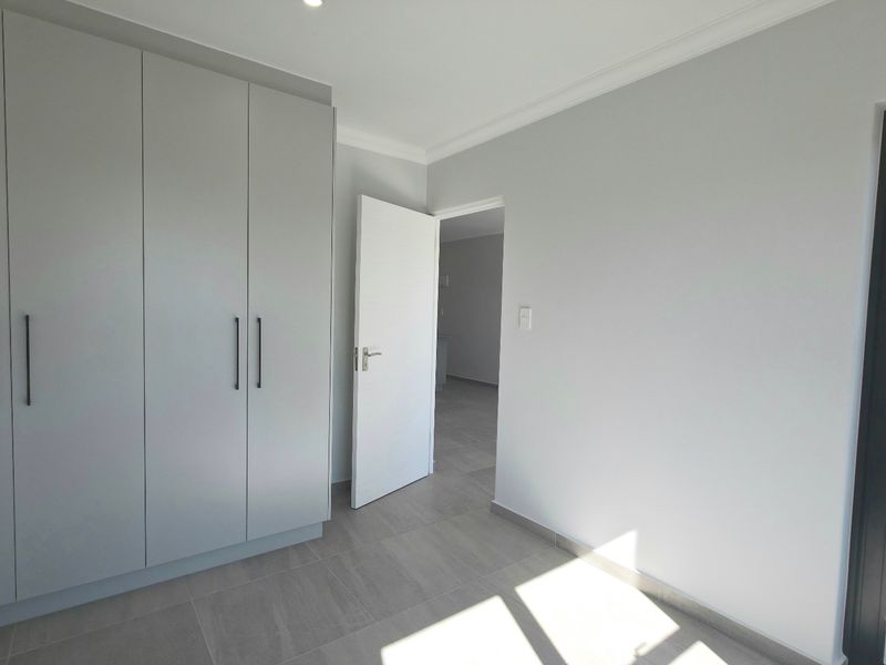 A bright, modern bedroom featuring neutral tiled flooring, built-in cupboards, and a sliding door leading to an outdoor area.