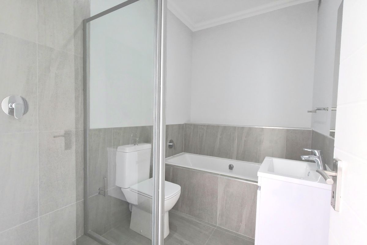 Modern bathroom featuring a glass-enclosed shower, built-in bathtub, wall-mounted toilet, and a sleek vanity basin with neutral porcelain tiling throughout.
