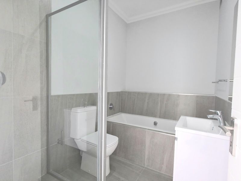 Modern bathroom featuring a glass-enclosed shower, built-in bathtub, wall-mounted toilet, and a sleek vanity basin with neutral porcelain tiling throughout.