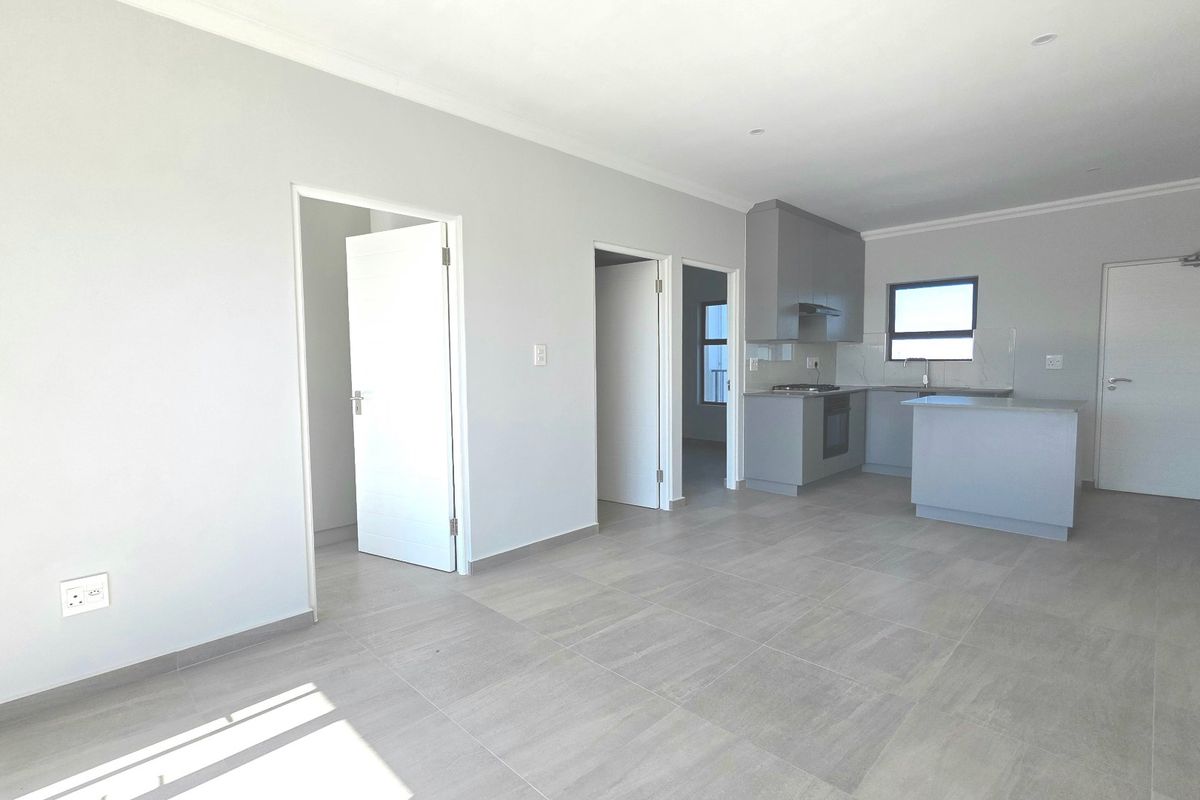 Spacious open-plan living area featuring modern grey kitchen cabinetry, integrated appliances, kitchen island, and neutral tiled flooring throughout.