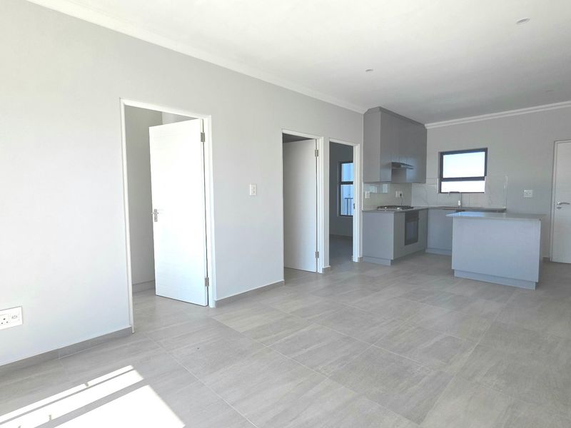 Spacious open-plan living area featuring modern grey kitchen cabinetry, integrated appliances, kitchen island, and neutral tiled flooring throughout.