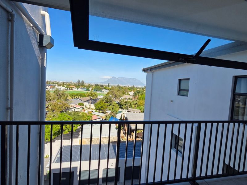 A balcony with a metal balustrade offering an elevated view of the surrounding neighborhood and distant mountain.